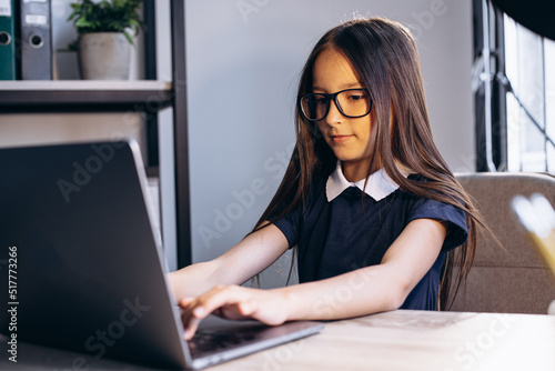 Little school girl studying on laptop at the desk