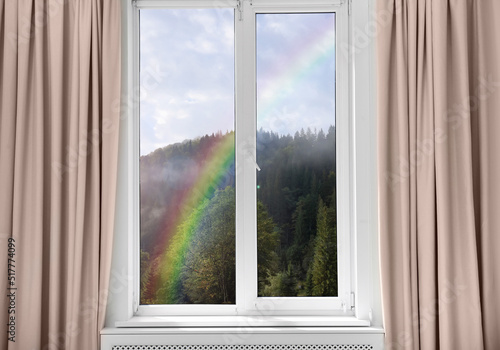 View of beautiful rainbow in mountains through window