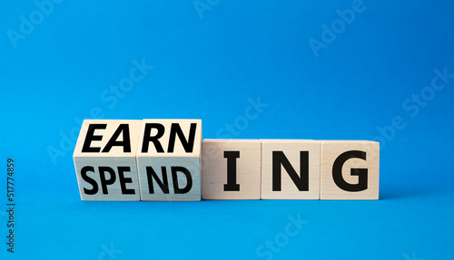 Earning and Spending symbol. Turned cubes with words Earning and Spending. Beautiful blue background. Business and Earning and Spending concept. Copy space
