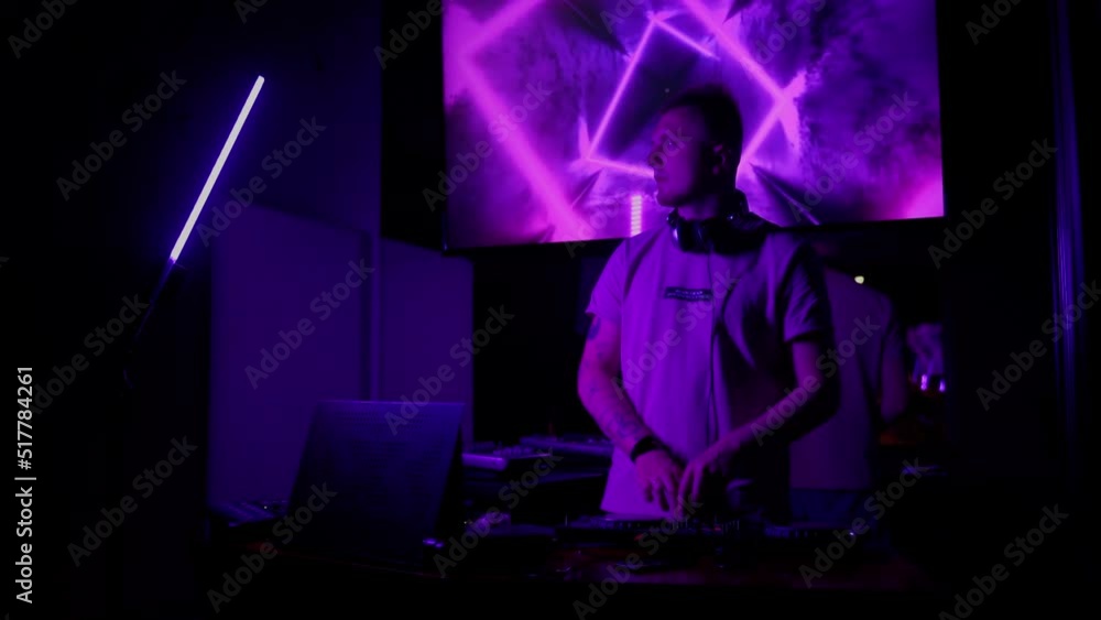 DJ in club working indoors in neon light. Caucasian male deejay person in nightclub using headphones, laptop and control console to mix audio music tracks list. Nightlife concept. Slow motion 4K video DJ in club working indoors in neon light. Caucasian male deejay person in nightclub using headphones, laptop and control console to mix audio music tracks list. Nightlife concept. Slow motion 4K video