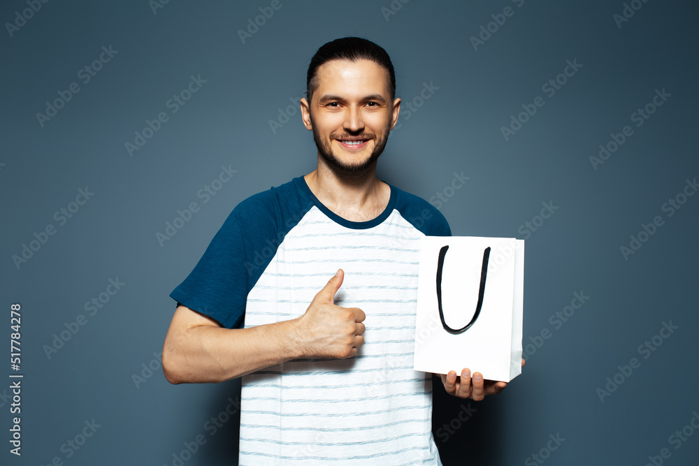 Studio portrait of young smiling man, holding a white bag and showing thumb up. Studio portrait of young smiling man, holding a white bag and showing thumb up.
