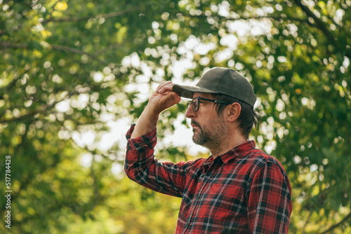 Portrait of male farmer wearing plaid shirt and trucker's hat in walnut fruit orchard looking at trees