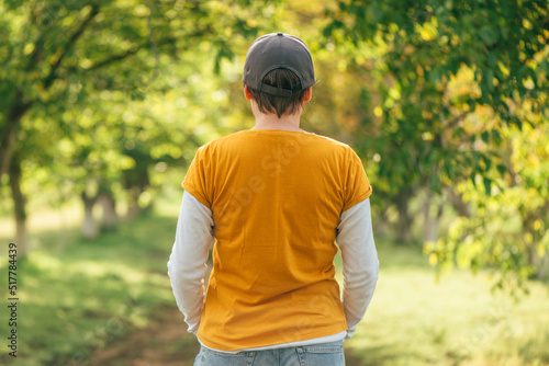 Rear view of female farmer wearing orange t-shirt and trucker's hat in walnut fruit tree orchard