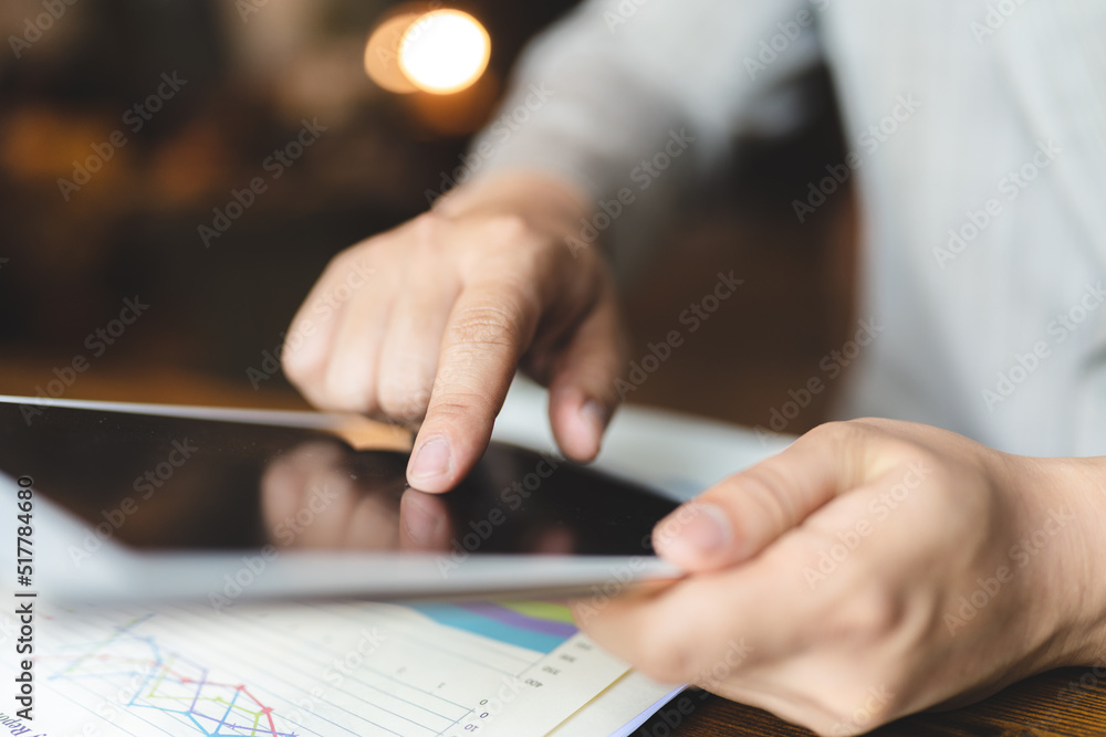 Fototapeta premium Hands of young man typing and working on digital tablet with financial and sales chart