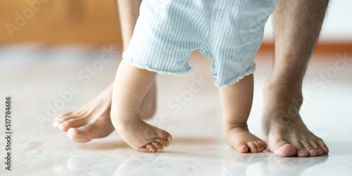 Baby learning to walk with father helping him learn at home by holding hand