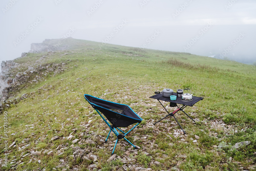 Hiking kitchen camping equipment stands on the mountain against the background of nature, a folding camping chair, camping furniture.