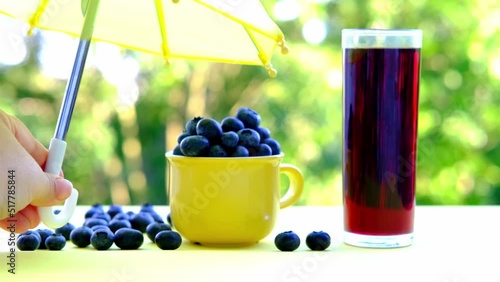 Vaccínium uliginosum, blue blueberries in yellow mug, glass of fresh juice on table in garden, plant of Heather family, green foliage, concept of healthy eating, vegan diet, raw food, healthy food photo