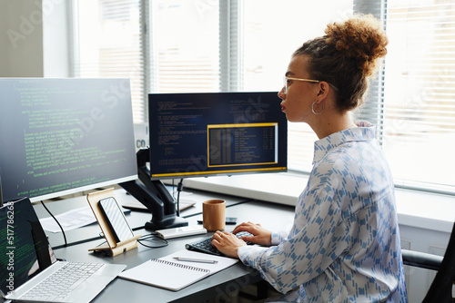 Young female IT specialist writing codes of new software on computer while sitting at her workplace at office photo