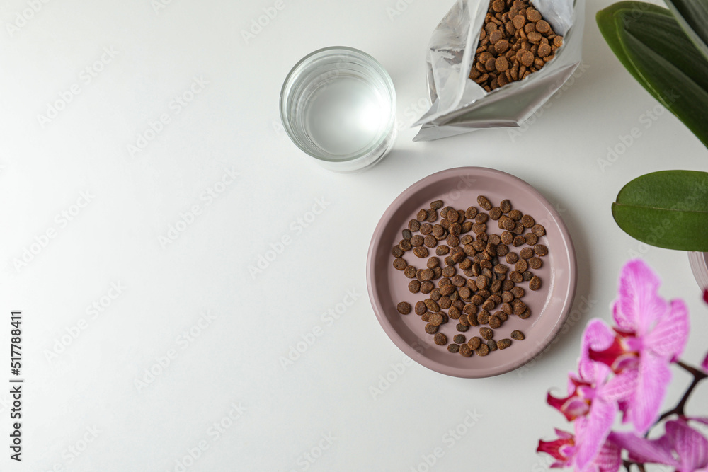 Dry cat food, glass of water and flowers on white table, flat lay. Space for text Dry cat food, glass of water and flowers on white table, flat lay. Space for text