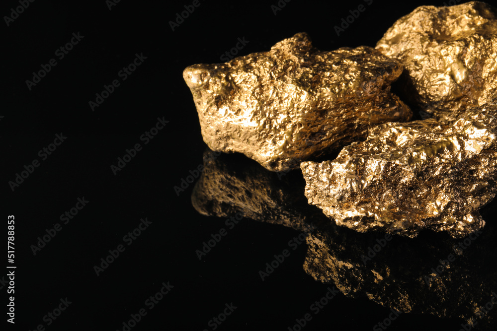 Obraz premium Gold nuggets on black reflective surface, space for text