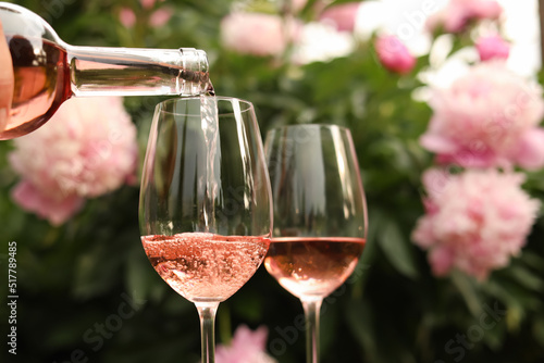 Fototapeta Naklejka Na Ścianę i Meble -  Pouring rose wine from bottle into glass against beautiful peonies, closeup