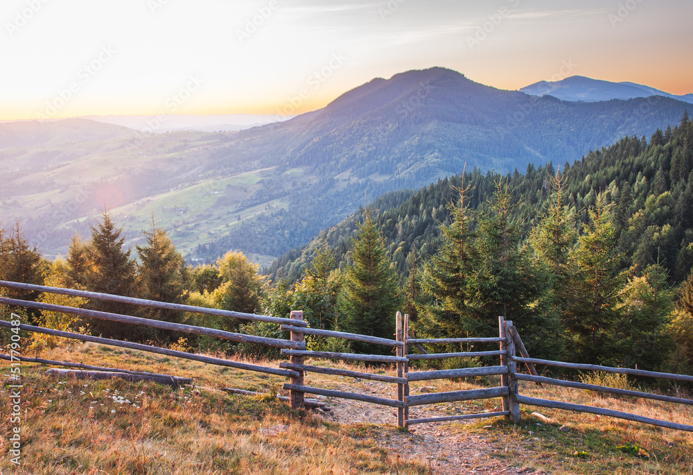 Sunrise in Ukrainian carpathians with pasture fence in foreground and waley on background. 