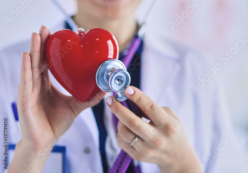 A doctor with stethoscope examining red heart, isolated on white background photo