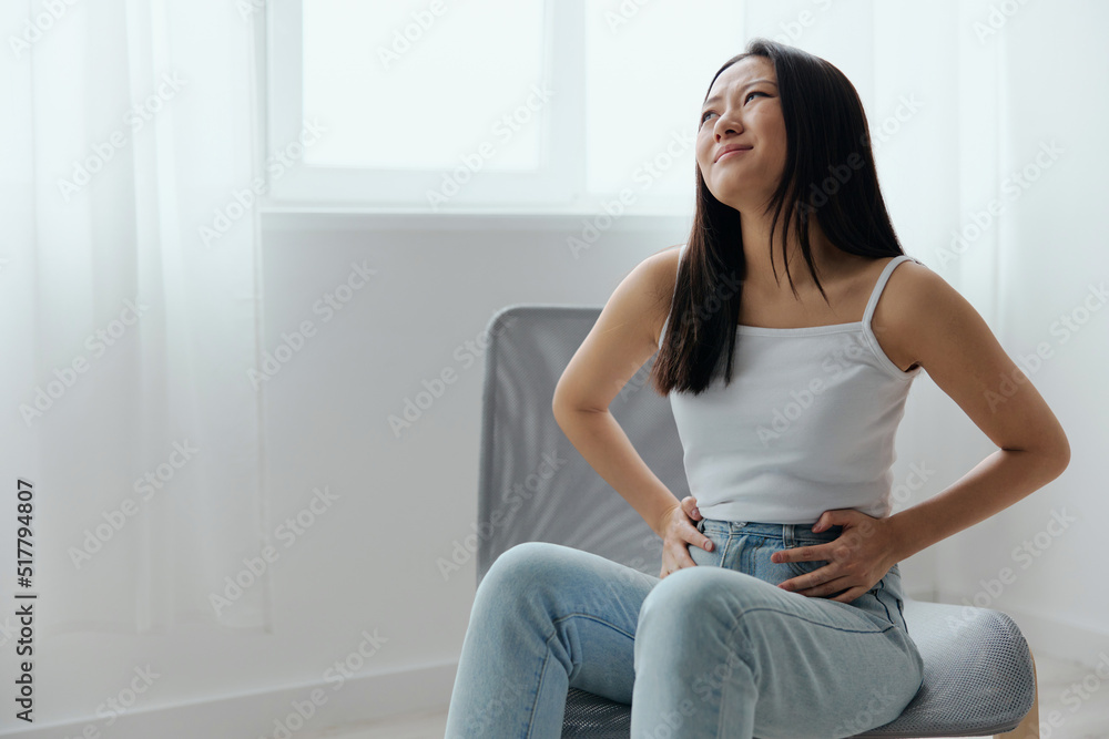 Stomach ulcer Gastritis. Tormented suffering tanned beautiful young Asian woman hold hands on stomach at home interior living room. Injuries Poor health Illness concept. Cool offer Banner Stomach ulcer Gastritis. Tormented suffering tanned beautiful young Asian woman hold hands on stomach at home interior living room. Injuries Poor health Illness concept. Cool offer Banner
