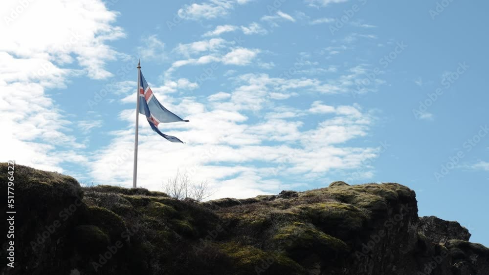Beautiful Icelandic flag waving on rocky cliff. Low angle view of national flag on mountain against blue cloudy sky. Concept of patriotism in Thingvellir National Park. Beautiful Icelandic flag waving on rocky cliff. Low angle view of national flag on mountain against blue cloudy sky. Concept of patriotism in Thingvellir National Park.