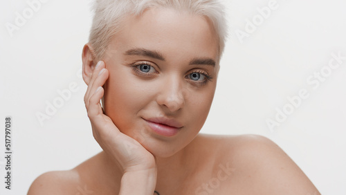 Good-looking young slim Caucasian woman with light hair looks at the camera resting her head on hand on white background   Face care concept