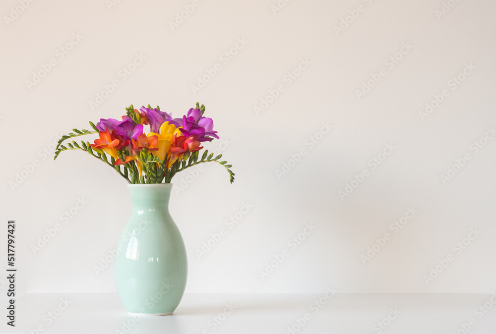 Close up of colourful freesia flowers in green vase against white background with copy space to right (selective focus) Close up of colourful freesia flowers in green vase against white background with copy space to right (selective focus)
