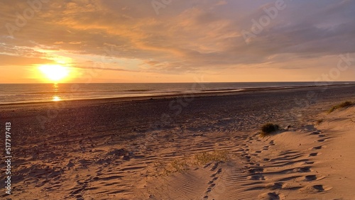 Schönes orangefarbenes Licht bei Sonnenuntergang an einem Strand an der Nordsee in Dänemark mit Fußspuren in Richtung Ozean