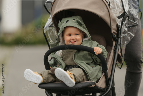 Obraz na płótnie A female toddler with her tongue out is sitting in the stroller on a cloudy day. A young girl in a baby carriage in a village green. w salonie