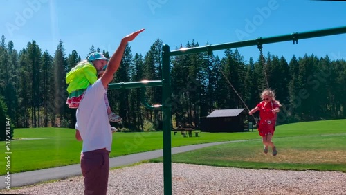 Father is playing with two daughters on the swings in the park during summer