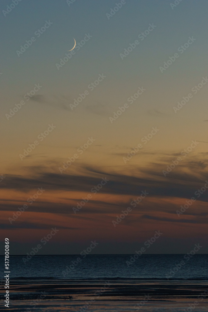 Crescent moon on twilight sky over beach with sea in evening with colorful sunlight after sunset Crescent moon on twilight sky over beach with sea in evening with colorful sunlight after sunset