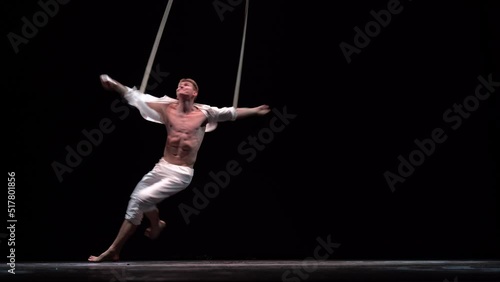 Muscular circus artist perform on the aerial straps on black background. Movement, strength concept photo