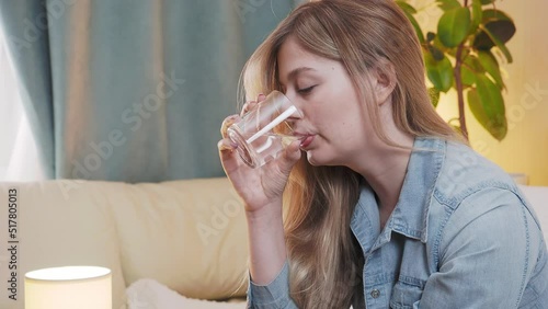 A young beautiful woman takes a pill and drinks water from a glass