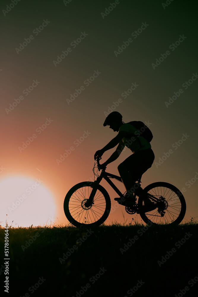 Fototapeta premium A cyclist riding a bike on a mountain at sunset