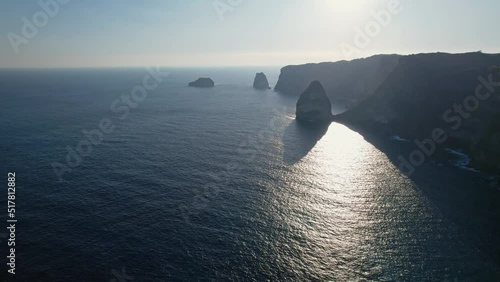 Aerial shot of rocky cliff. Indian ocean shore. Beautiful nature and travel summer vacation concept. Drone fly along coastline at sunset. Nusa Penida Island in Bali