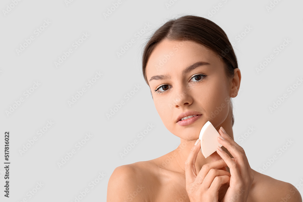 Pretty young woman with makeup sponge on grey background Pretty young woman with makeup sponge on grey background