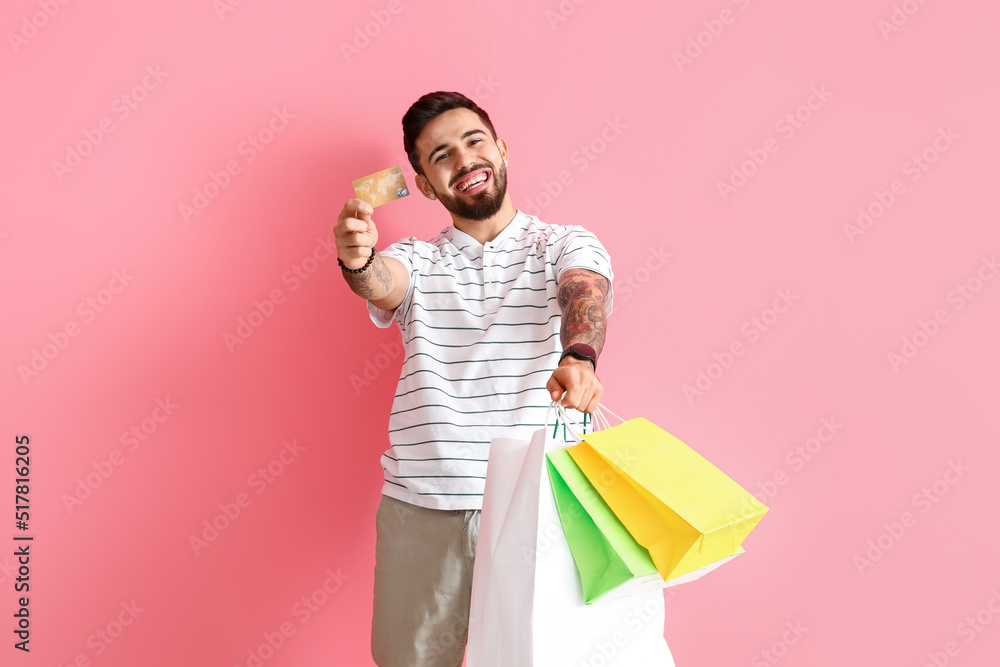 Handsome man with credit card and shopping bags on pink background Handsome man with credit card and shopping bags on pink background