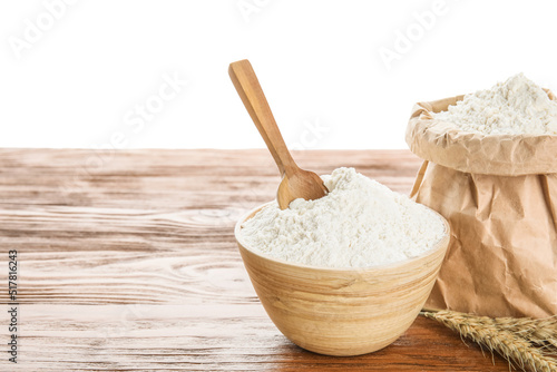 Bowl, paper bag with flour, scoop and wheat ears on wooden table against white background