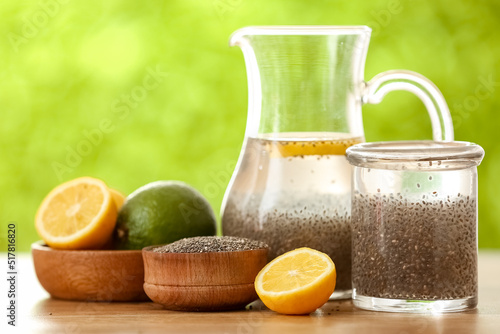 Glass of water with chia seeds, jug, bowls and citrus fruits on table outdoors