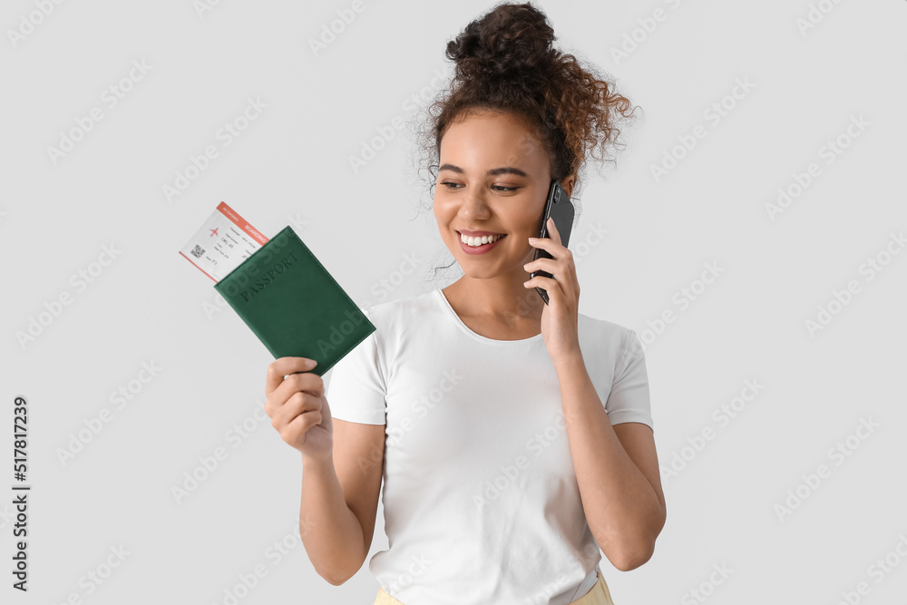 Female African-American tourist with passport talking by mobile phone on light background Female African-American tourist with passport talking by mobile phone on light background