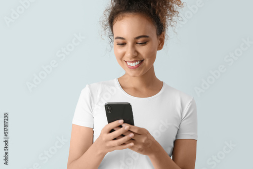 Female African-American tourist using mobile phone on light background