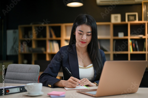Attractive young-adult Asian businesswoman is focused on her task at the office desk.