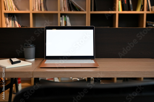 Laptop white screen mockup on a wood table in coffee shop co-working space or library. © bongkarn