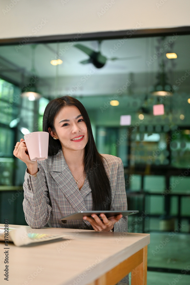 Attractive asian businesswoman holding tablet and a cup of coffee.