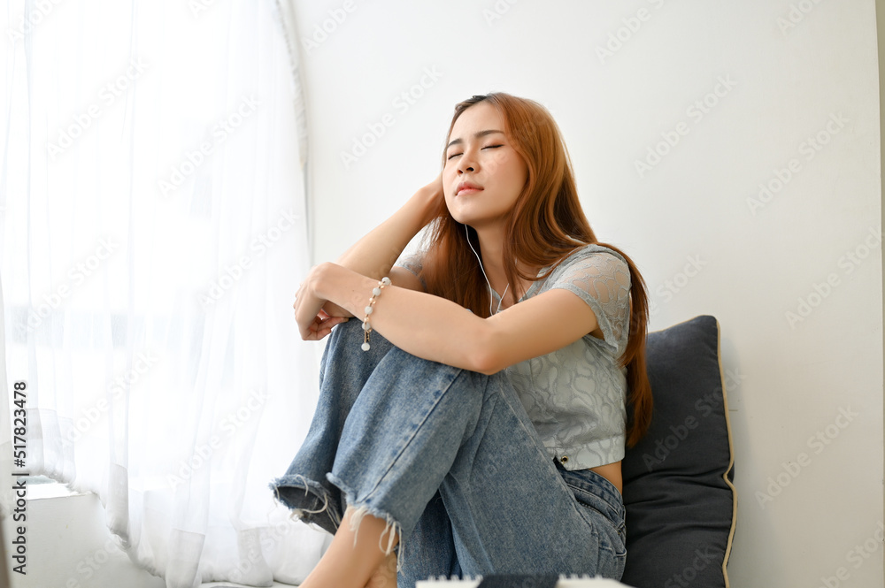 Tired and unhappy millennial Asian woman sitting in living room, feeling upset with herself Tired and unhappy millennial Asian woman sitting in living room, feeling upset with herself