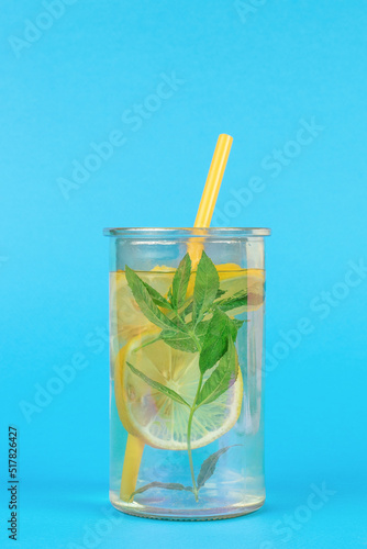 A large glass with lemon, mint and cucumber and a cocktail tube on a blue background.