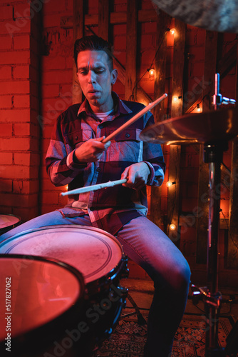 Serious male player with wooden drumstick playing drums on stage during live performance in dark club