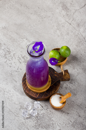 iced butterfly pea flower tea or teh bunga telang with glass bottle on wooden coaster and white background texture photo