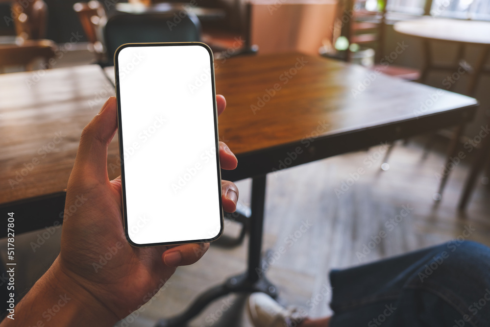 Mockup image of a man holding black mobile phone with blank white screen in cafe Mockup image of a man holding black mobile phone with blank white screen in cafe