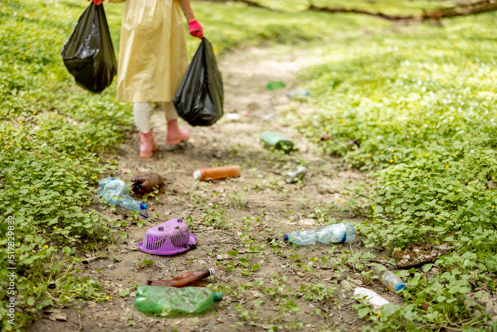 Fototapeta premium Scattered plastic garbage on dried river in the woods and woman going with bags on background. Problem of ecology and environmental pollution