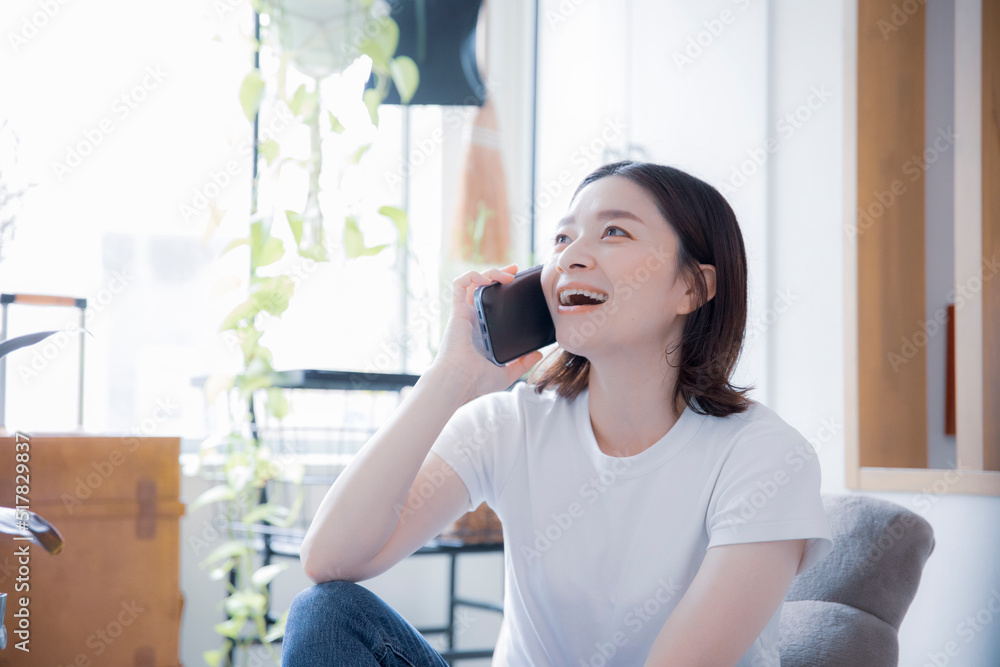 明るい室内でスマートフォンで笑顔で通話する日本人女性 明るい室内でスマートフォンで笑顔で通話する日本人女性