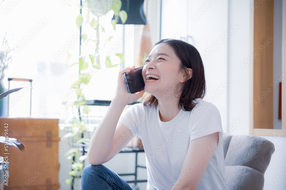 明るい室内でスマートフォンで笑顔で通話する日本人女性 明るい室内でスマートフォンで笑顔で通話する日本人女性