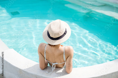 Happy woman in white swimsuit swimming in luxury pool hotel, young female with hat enjoy in tropical resort. Relaxing, summer travel, holiday, vacation and weekend concept