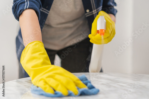Cleaning hygiene, close up hand of maid, waitress woman wearing yellow protective gloves while cleaning on wood table, use blue rag wiping to dust and spray in restaurant. Housekeeping cleanup,cleaner