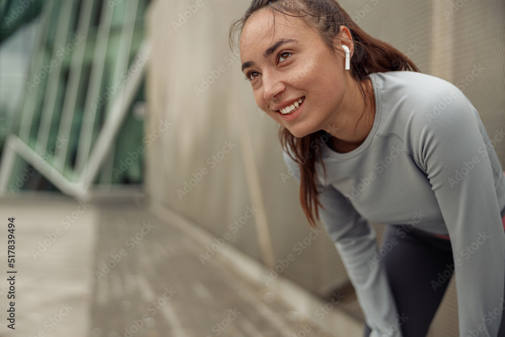Young smiling woman in sportswear resting after run in city leaning against the wall Young smiling woman in sportswear resting after run in city leaning against the wall