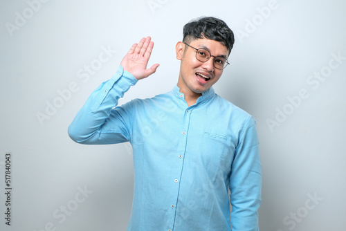 Young handsome asian man waiving saying hello happy and smiling, friendly welcome gesture